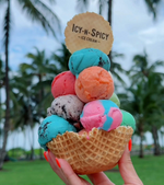 Colorful ice cream tower with 'Icy-N-Spicy' waffles held in a hand against a blurred outdoor background.